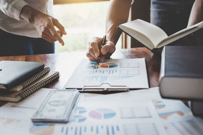 Midsection of colleagues working over graph at desk in office