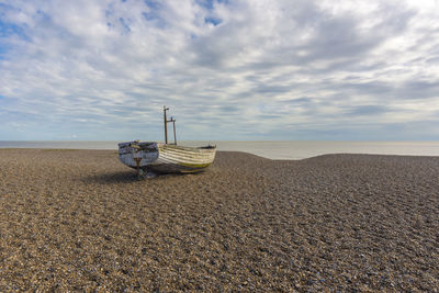 Abandoned boat on beach against cloudy sky