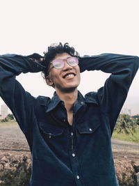 Portrait of smiling young man standing on field against sky