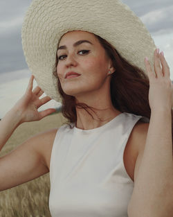 Portrait of beautiful young woman wearing hat standing on beach