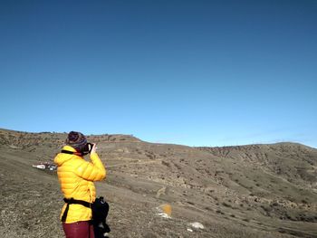 Rear view of woman standing on mountain against clear blue sky