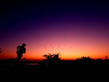 Silhouette man standing on field against sky during sunset