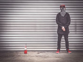 Man wearing scarf and sunglass standing with red paint against shutter