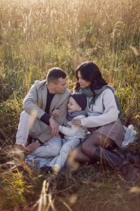 Stylish family with a boy child sits on a field in the dry grass in autumn