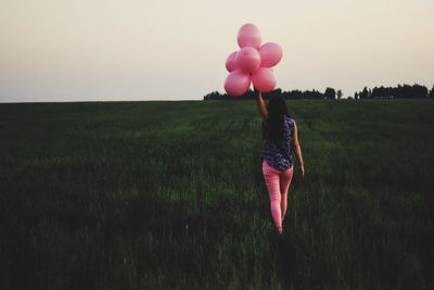 Full length of woman with pink balloons walking on field against sky