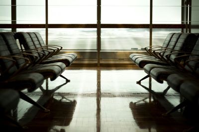 Chairs in airport departure area against glass window