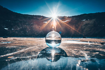 Reflection of crystal ball on water against sky during sunset