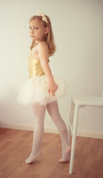 Ballet dancer standing on wooden floor against wall