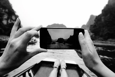 Cropped image of woman photographing sea through smart phone while sitting on boat