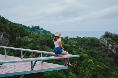 Woman sitting by railing against sky