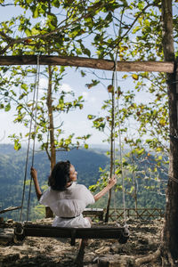 Rear view of woman sitting on sidewalk in forest