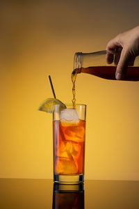 Close-up of hand holding drink against orange background