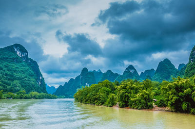 River by green mountains against cloudy sky