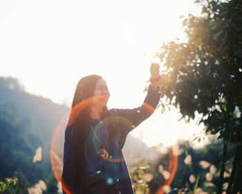 Smiling woman by tree against sky on sunny day