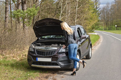 Side view of woman by breakdown car on road