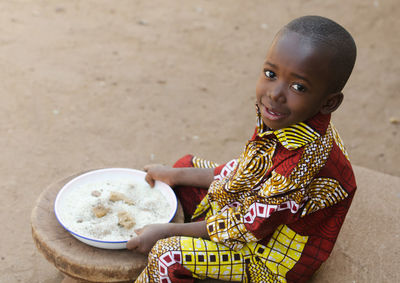 High angle portrait of cute boy holding plate sitting outdoors