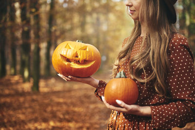 Midsection of woman holding jack o lantern and pumpkin during autumn