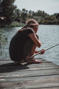 Girl fishing while crouching on pier