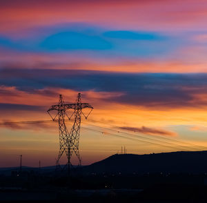 Silhouette electricity pylon against romantic sky at sunset