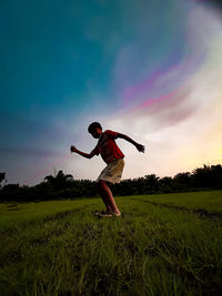 Full length of man with arms raised on field against sky during sunset