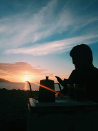 Silhouette man using smart phone against sky during sunset