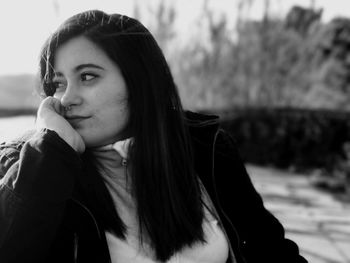 Young woman with hand on chin looking away while sitting outdoors