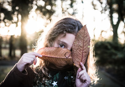 Portrait of girl holding dry leaves in park during sunset