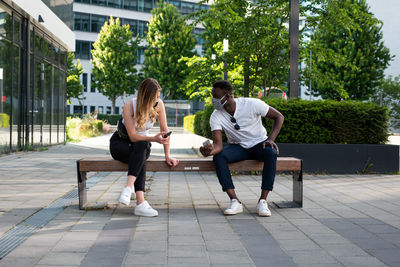 Full length of woman with man sitting on bench against trees