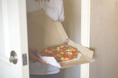 Midsection of man holding pizza box at home