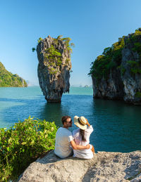 Rear view of woman sitting on rock by sea against sky