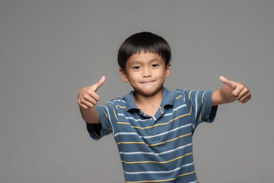 Portrait of boy gesturing thumbs up sign against gray background