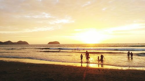 Silhouette people on calm beach at sunset