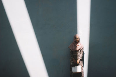 Portrait of young woman standing against wall