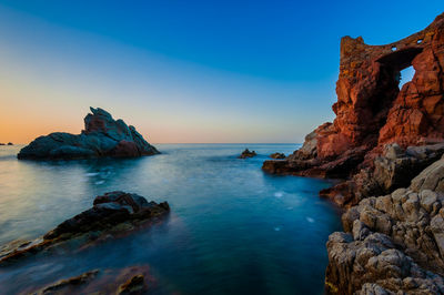 Rock formation in sea against clear blue sky