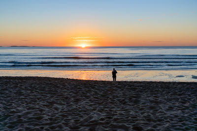 Silhouette woman walking at beach against sky during sunset