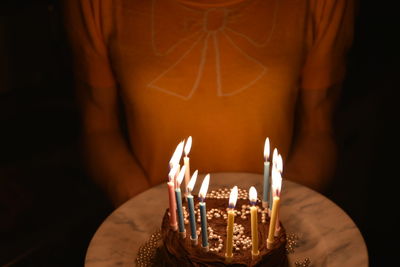Midsection of woman holding illuminated birthday cake