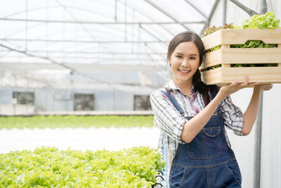 Portrait of smiling woman holding container with vegetable at farm