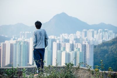 Rear view of man standing on mountain against cityscape