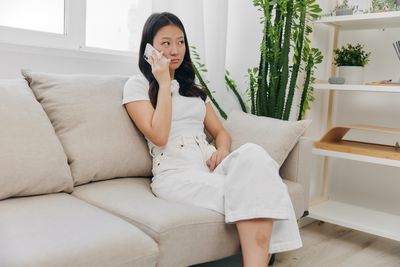 Young woman using mobile phone while sitting on sofa at home