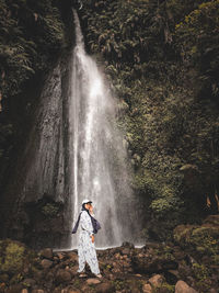 Woman standing by waterfall against trees