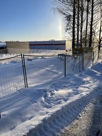 Snow covered field by fence against sky