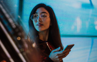 Close-up of young woman using mobile phone standing outdoors at night