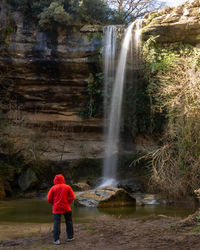 Rear view of person standing by salt del purgatori waterfall in forest