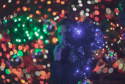 Young woman standing amidst illuminated christmas tree at night