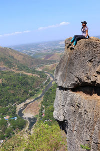 Woman sitting on cliff against sky