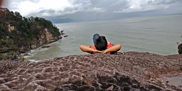 Man lying on cliff against sea