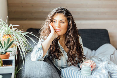Thoughtful young woman looking away while having coffee on bed at home