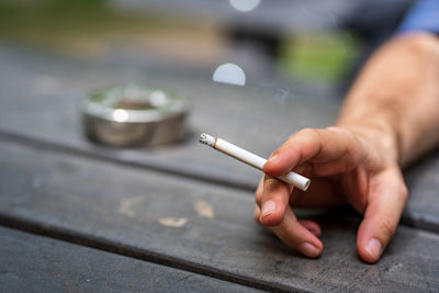 Cropped hand of man holding cigarette on table