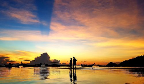 Silhouette people on sea against dramatic sky during sunset