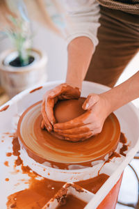 High angle of crop person in casual clothes making handmade pottery using special equipment while working in light contemporary studio